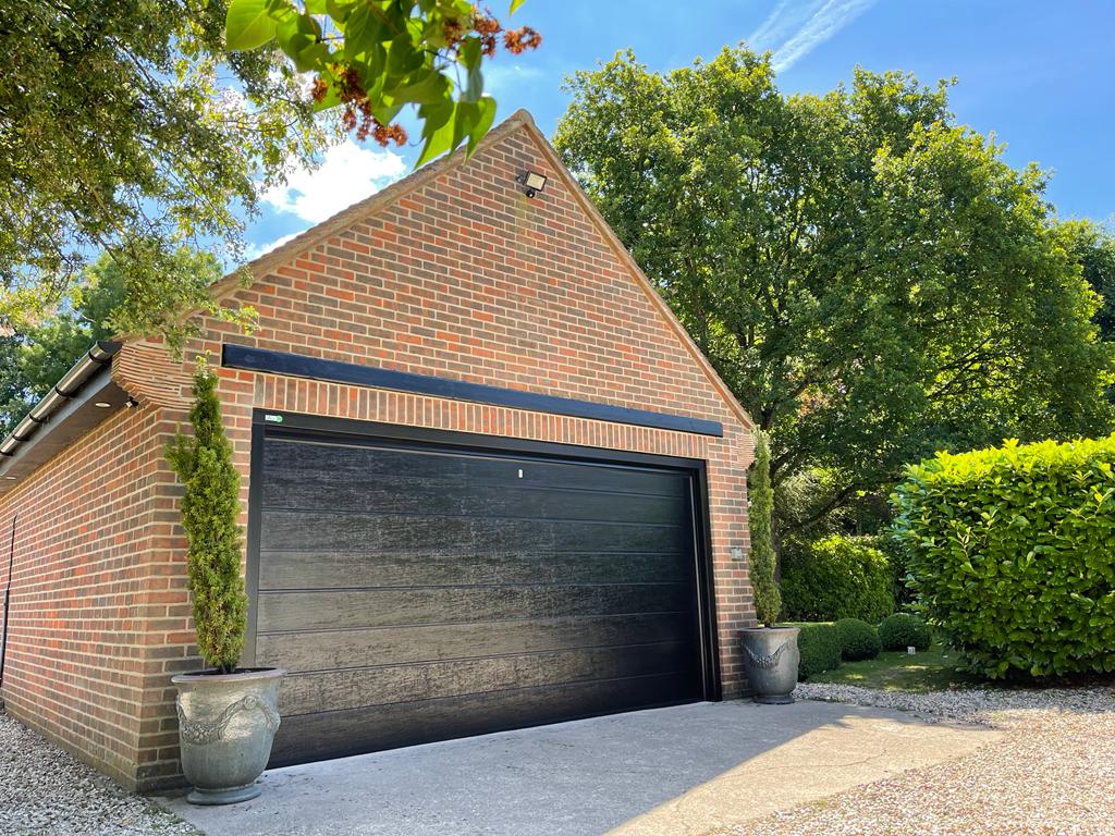 Detached brick garage building with sectional garage doors in jet black.