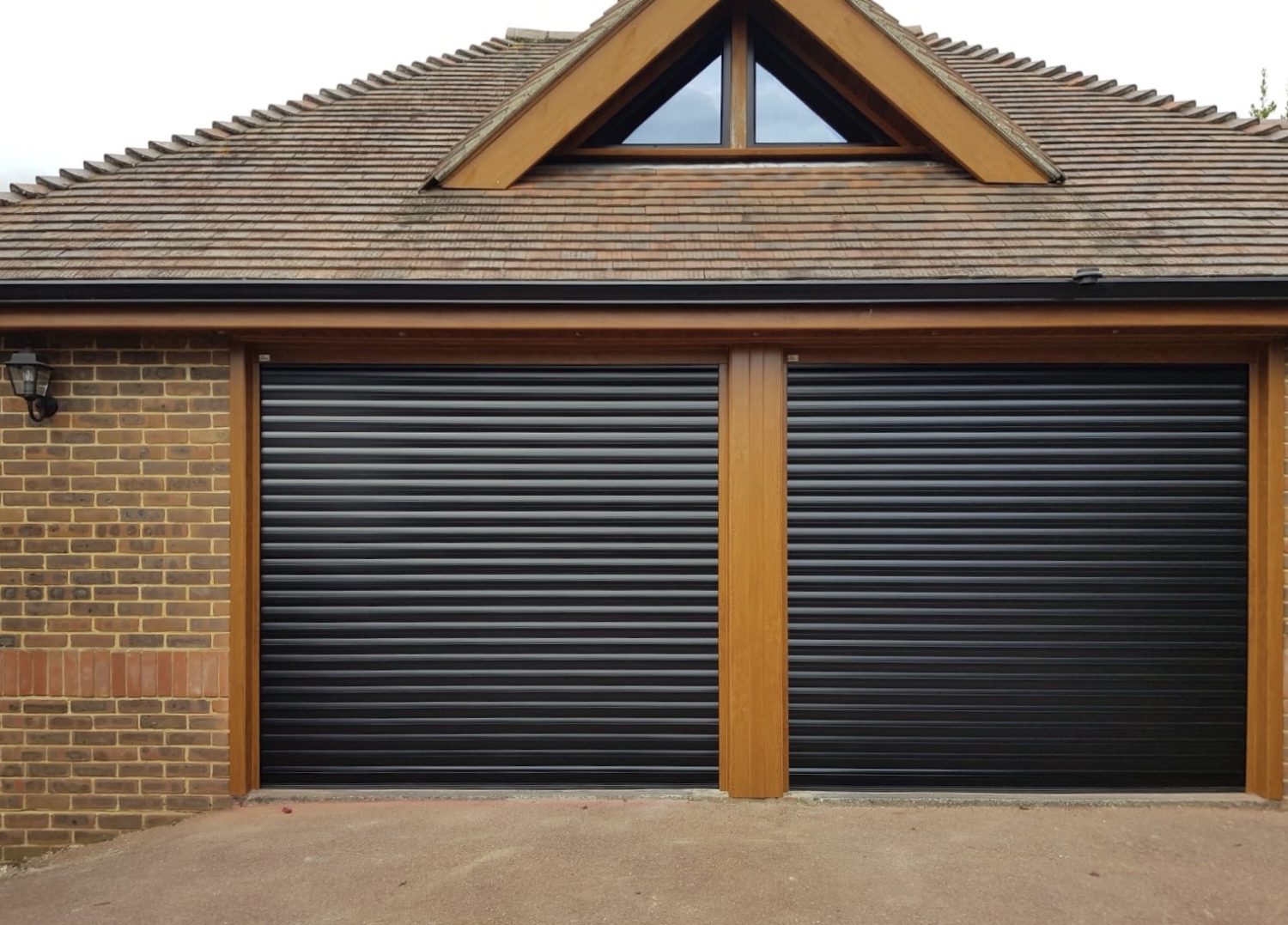 Double garage building with apex feature window and newly fitted roller garage doors in jet black.