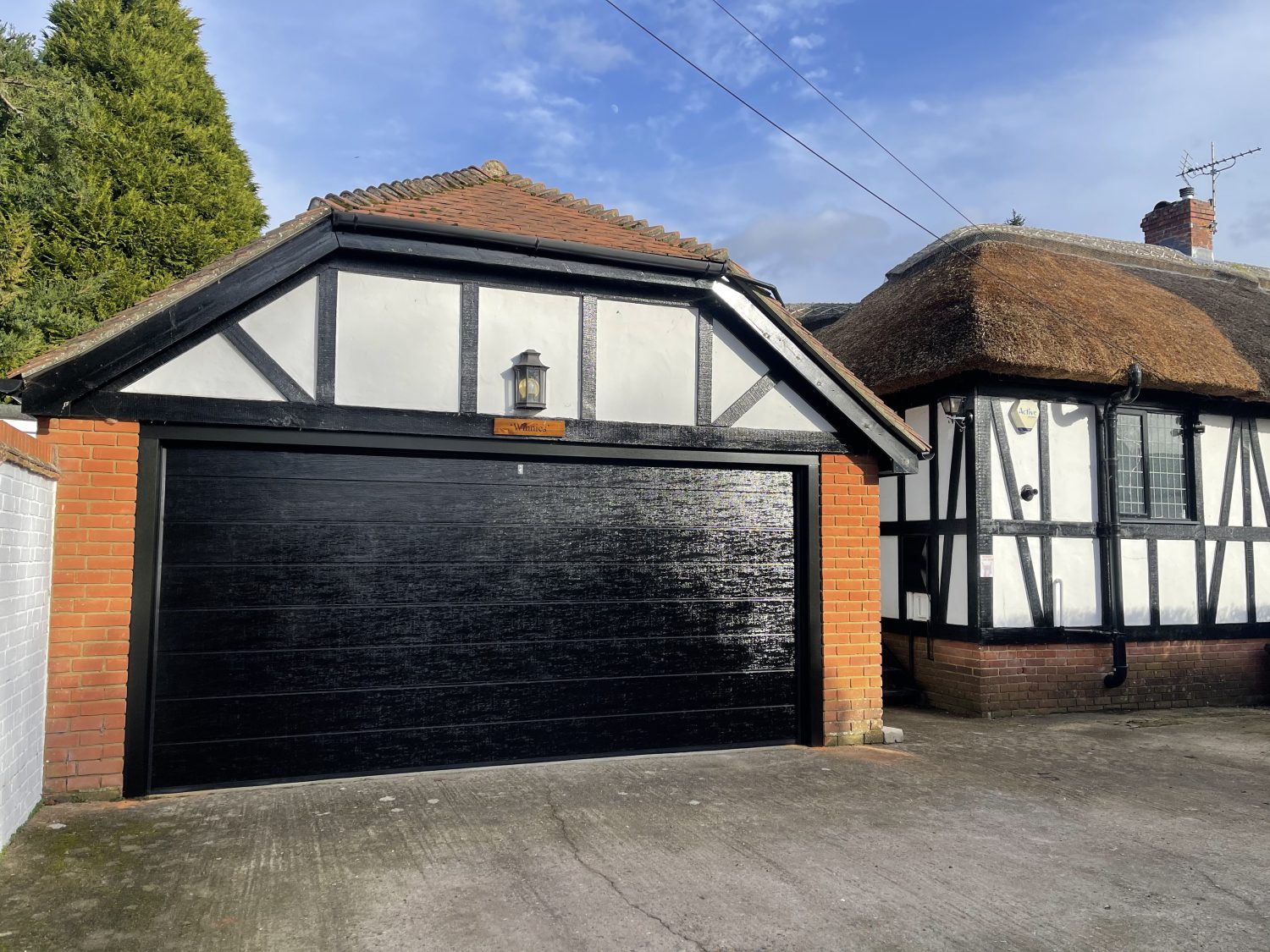 Detached garage building next to a thatched cottage with black sectional garage door.