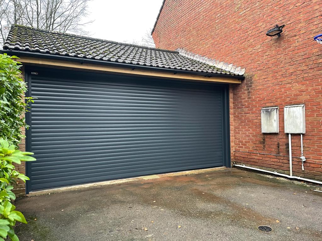 Double garage with a roller garage door in dark grey.