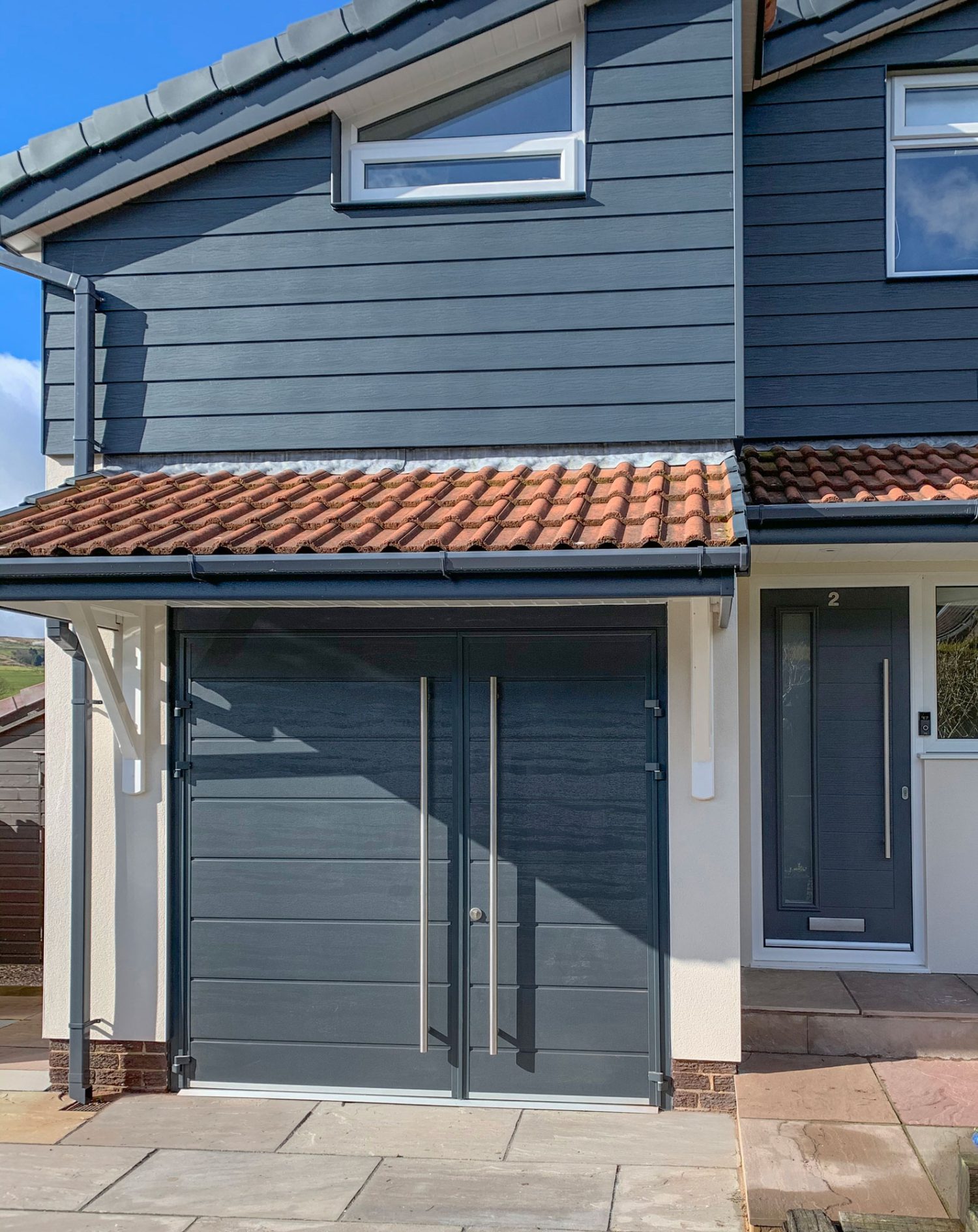 Side hung garage door in grey, matching the grey panelling of the house with a matching composite front door.