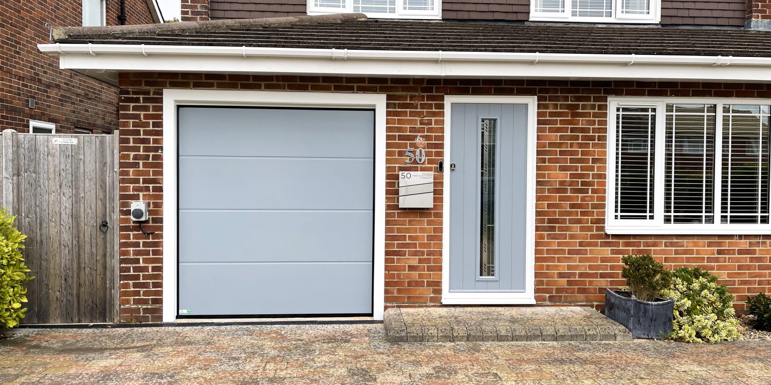 Matching dove grey sectional garage door and composite front door in a surburban estate.