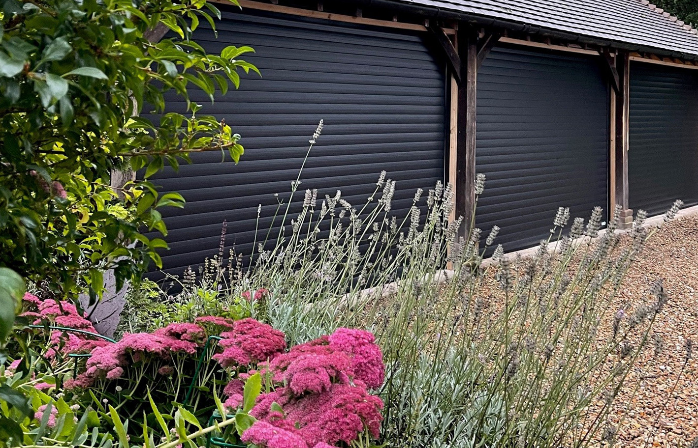Detached garage building with three seperate black garage doors with summer flowers in the foreground.