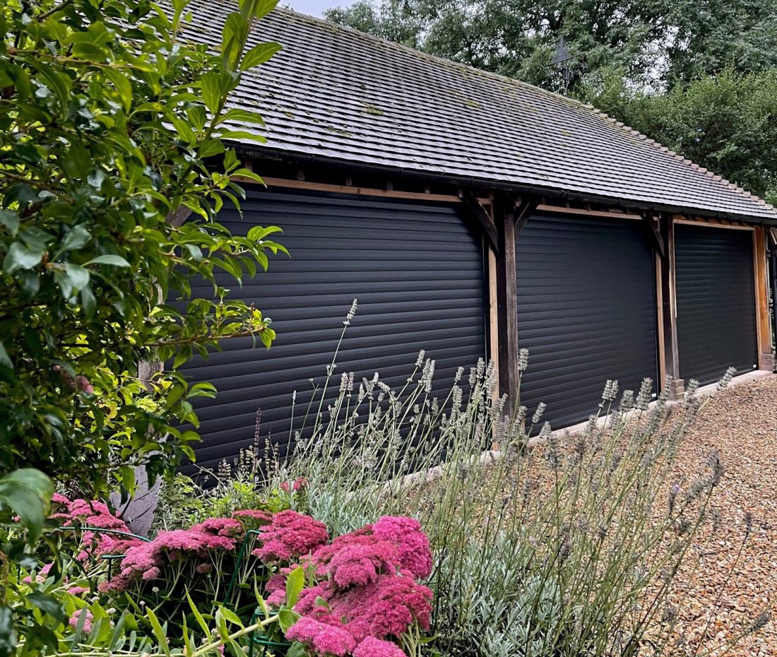 Detached garage building with three seperate black garage doors with summer flowers in the foreground.