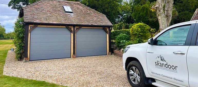 Skandoor vehicle outstide a detached double garage with grey doors.