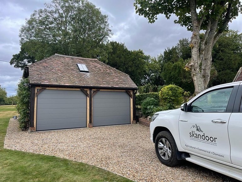 Sign written Skandoor vehicle in front of a detached garage building with sectional grey doors.
