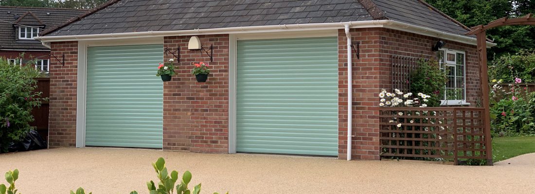 Detached garage building with two roller garage doors in Chartwell green in summertime surrounded by trellis and flowers.