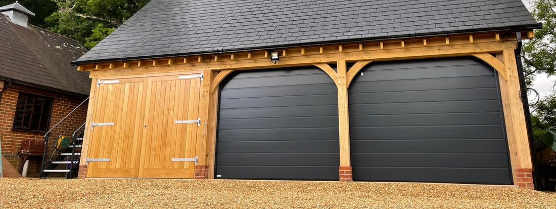 Detached garage building with timber frame and double jet black sectional garage doors.