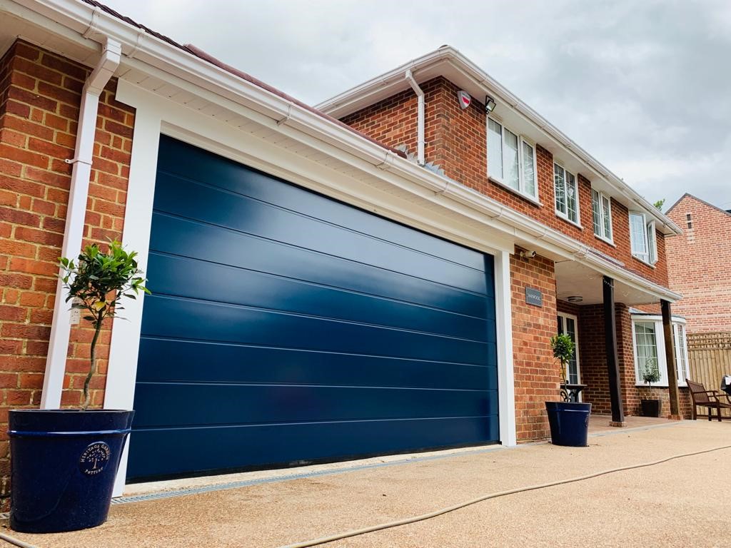 Substantial and attractive home in a surburban estate with a large blue sectional garage door and two olive trees either side of the building.